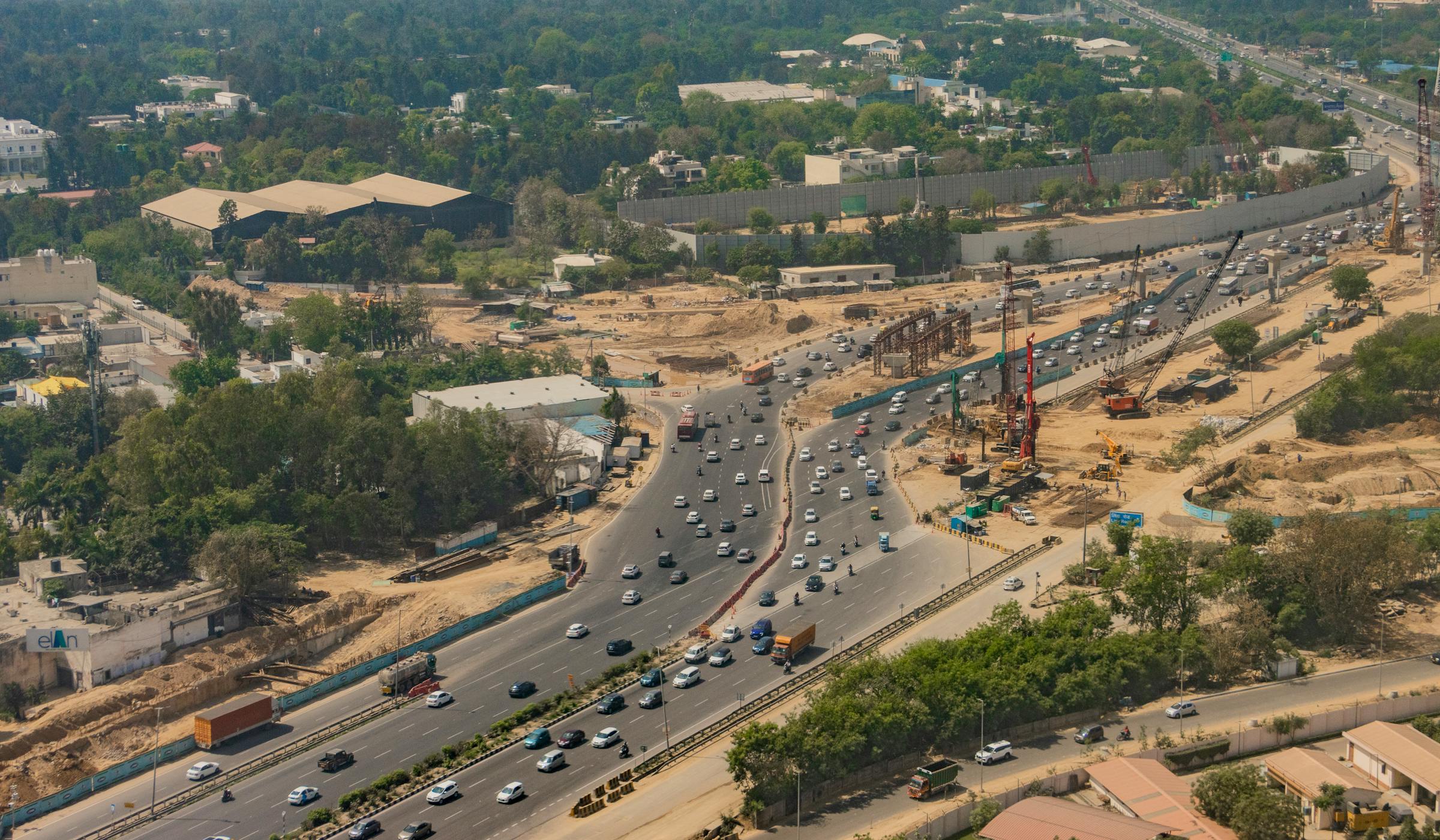 Aerial view of a major expressway interchange under construction in Delhi, with active traffic and earthworks