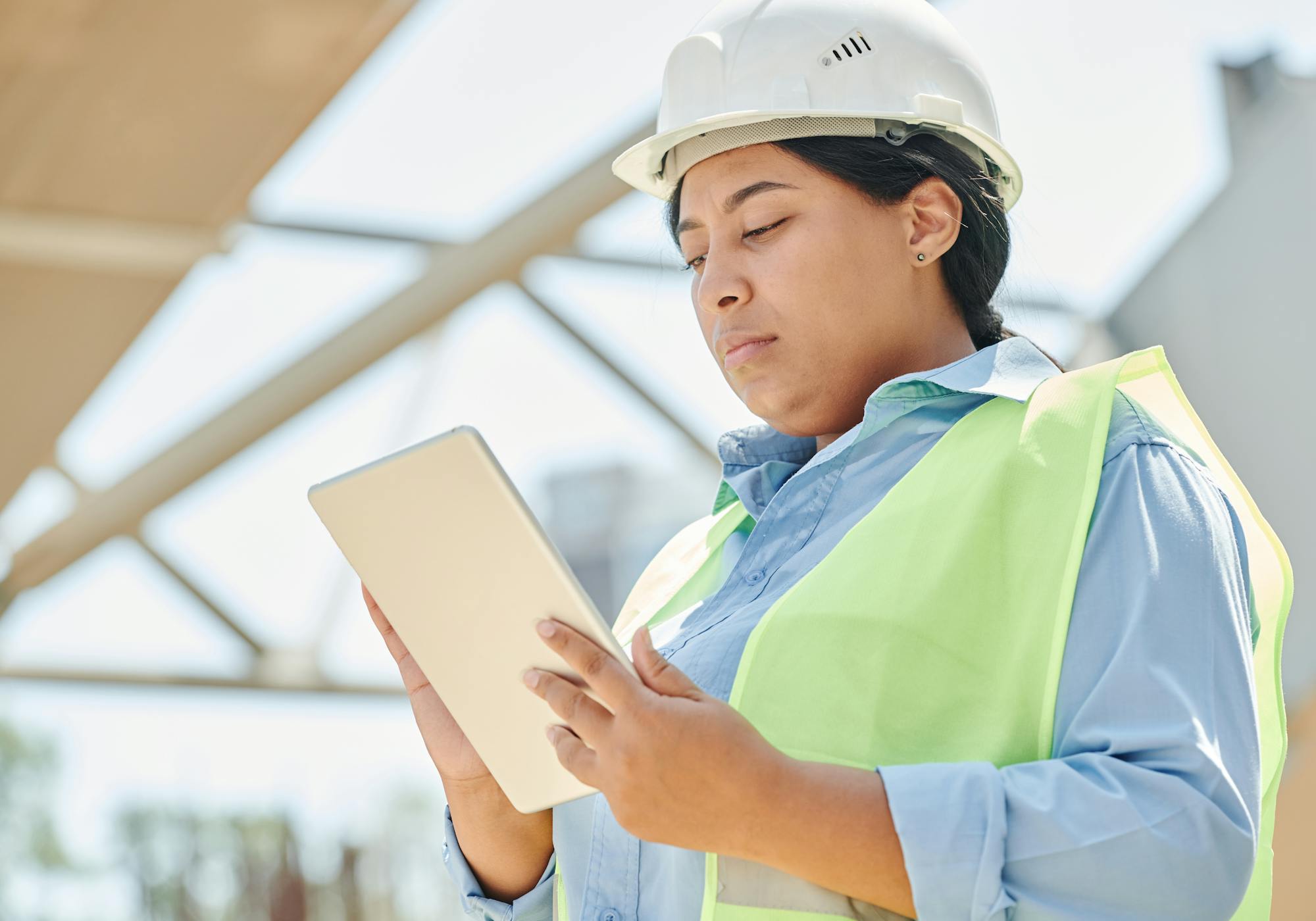 Site engineer in hard hat reviewing a tablet at a steel-framed construction site